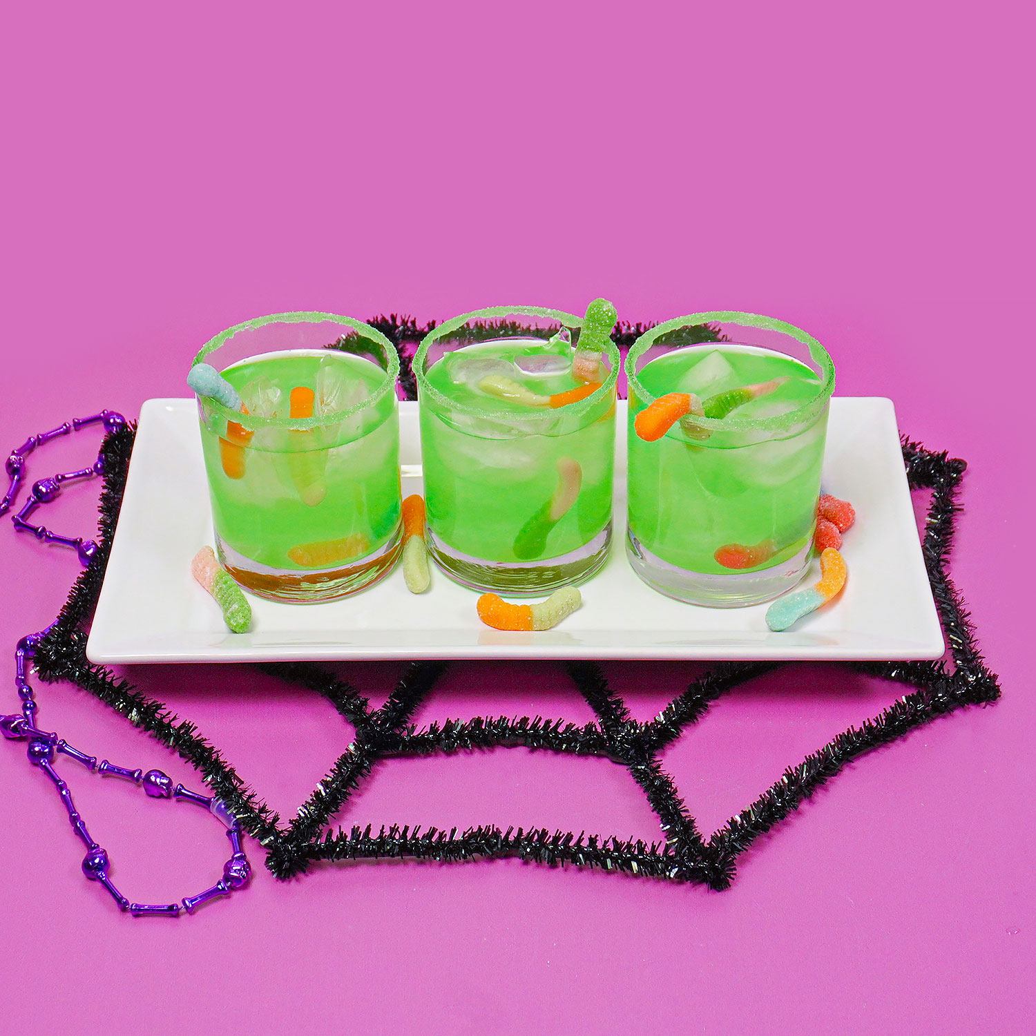 three neon green drinks with gummy worms on a Halloween background
