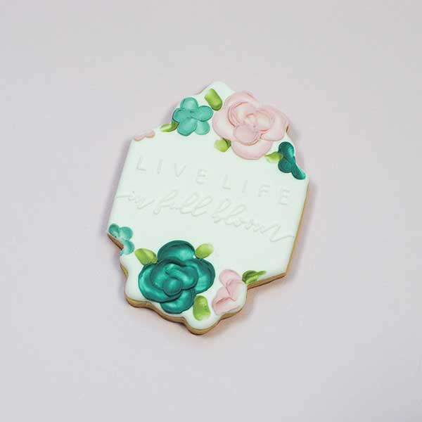 floral plaque cookies flooded with a white royal icing base. medium peak royal icing color in vibrant colors and applied with a palette knife to create flowers. White on white spring quote written live life in full bloom.