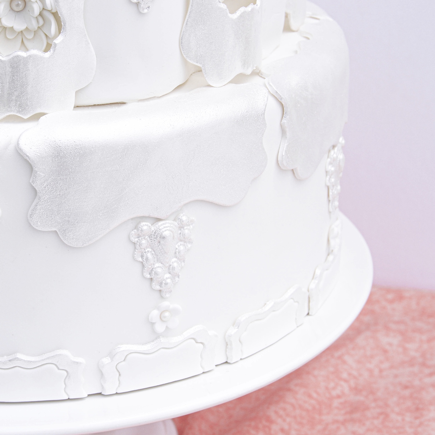 Bottom tier of fondant covered cake adorned with nora cutter frames covered in pearl luster dust and fondant pendants and blossom flowers.