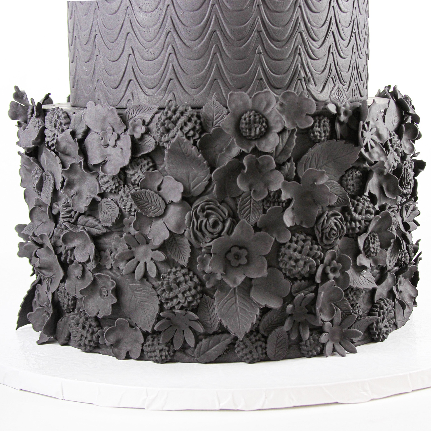 The third tier of this three tier black fondant cake is covered in 3d fondant florals and leaves designs