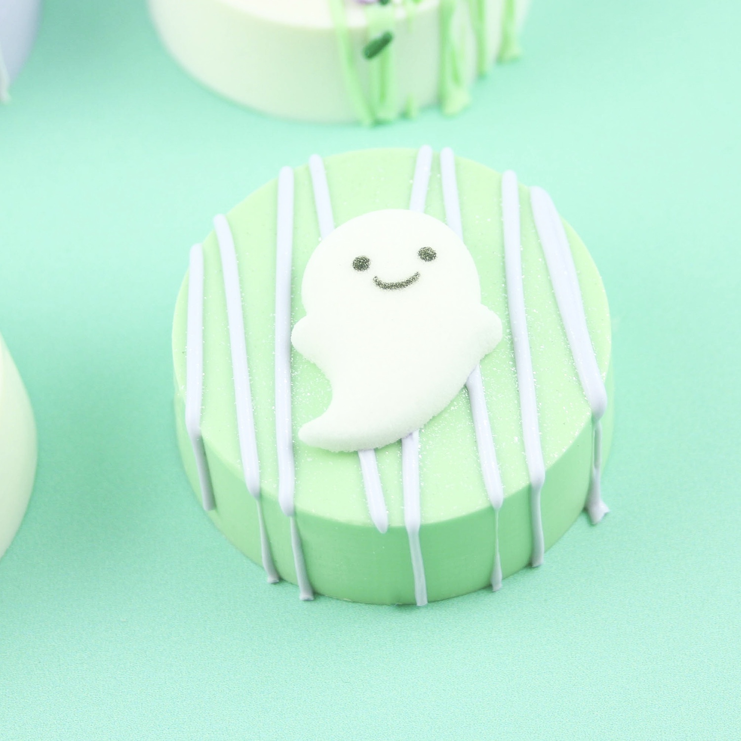 Green Chocolate molded sandwich cookie with white chocolate drizzle, sugar ghost and jewel dust.