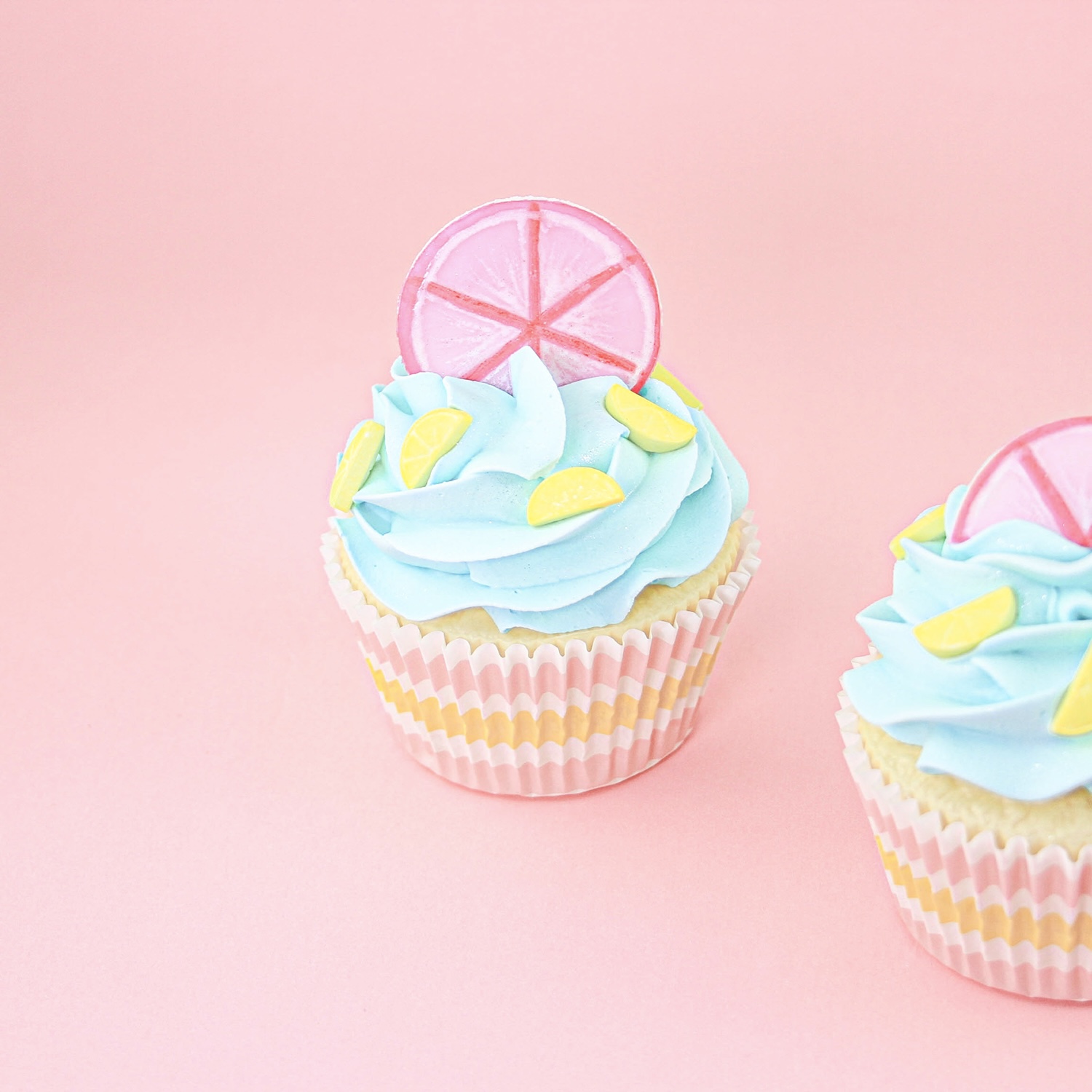 Blue buttercream swirled cupcake with a hand painted pink lemon slice fondant topper and lemon sprinkles.