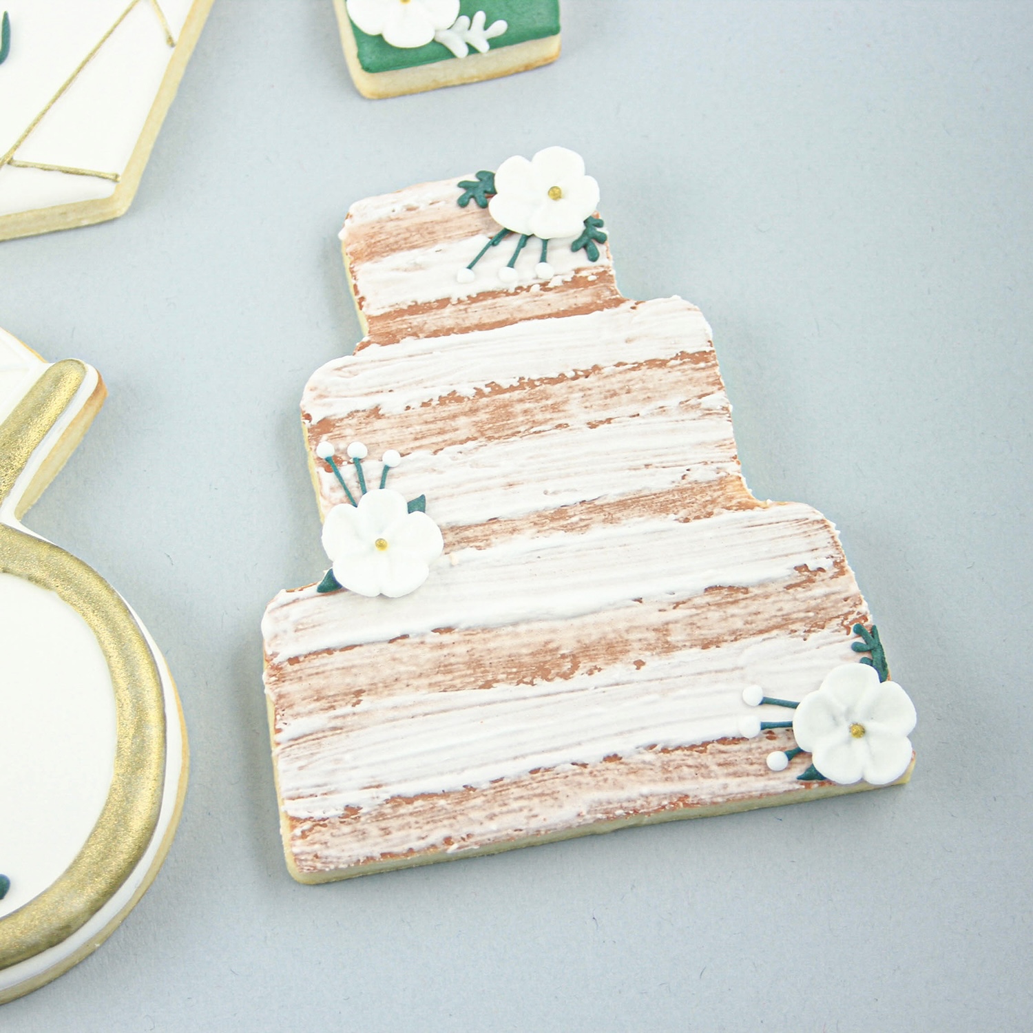 Wedding Cake cookie deocrated in royal icing to resemble a 3 tiered naked wedding cake and adorned with white royal icing flowers