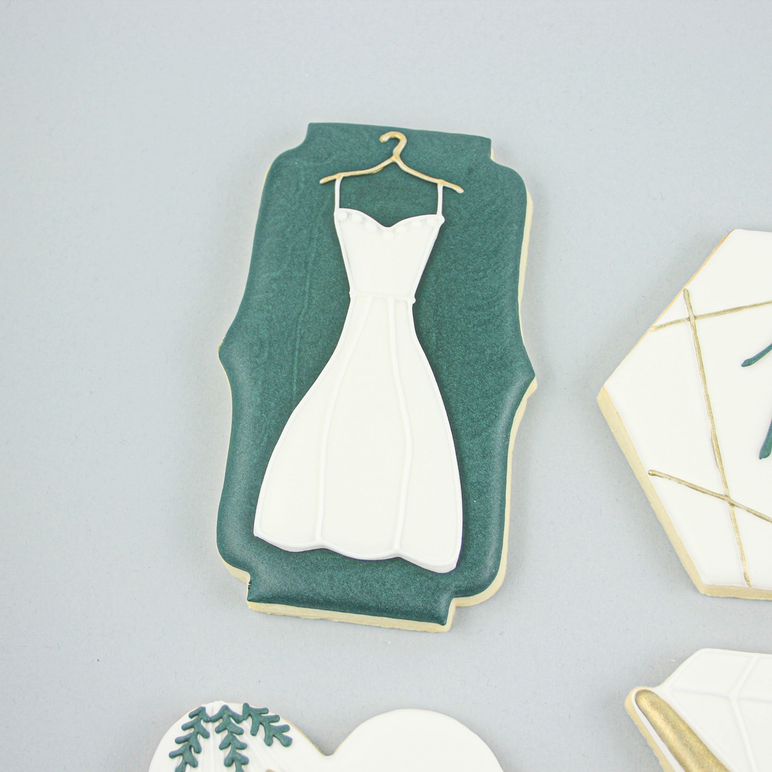 Green royal icing plaque cookie adorned with a white wedding dress hanging on a hanger. 