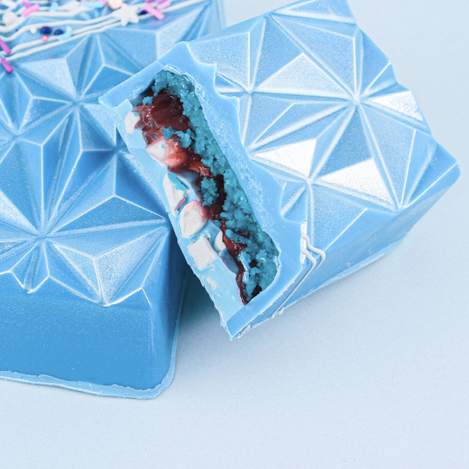 Geometric cakesicles with a blue candy outer shell. the inside is filled with cakesicle dough, raspberry filling and marshmallows.