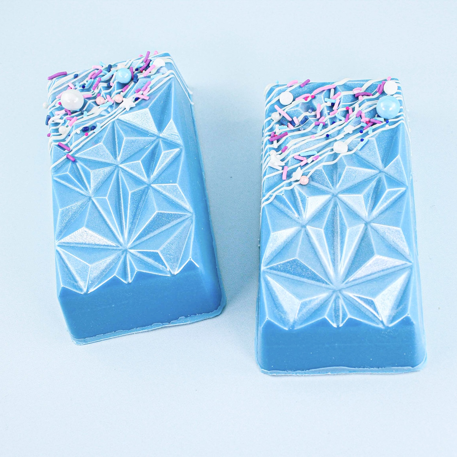 Geometric molded bars with a blue outer shell. inside is filled with cake dough, rapsberry filling and marshmallows.  THe outside with brushed in luster dust and drizzled with white candy coating and sprinkles. 