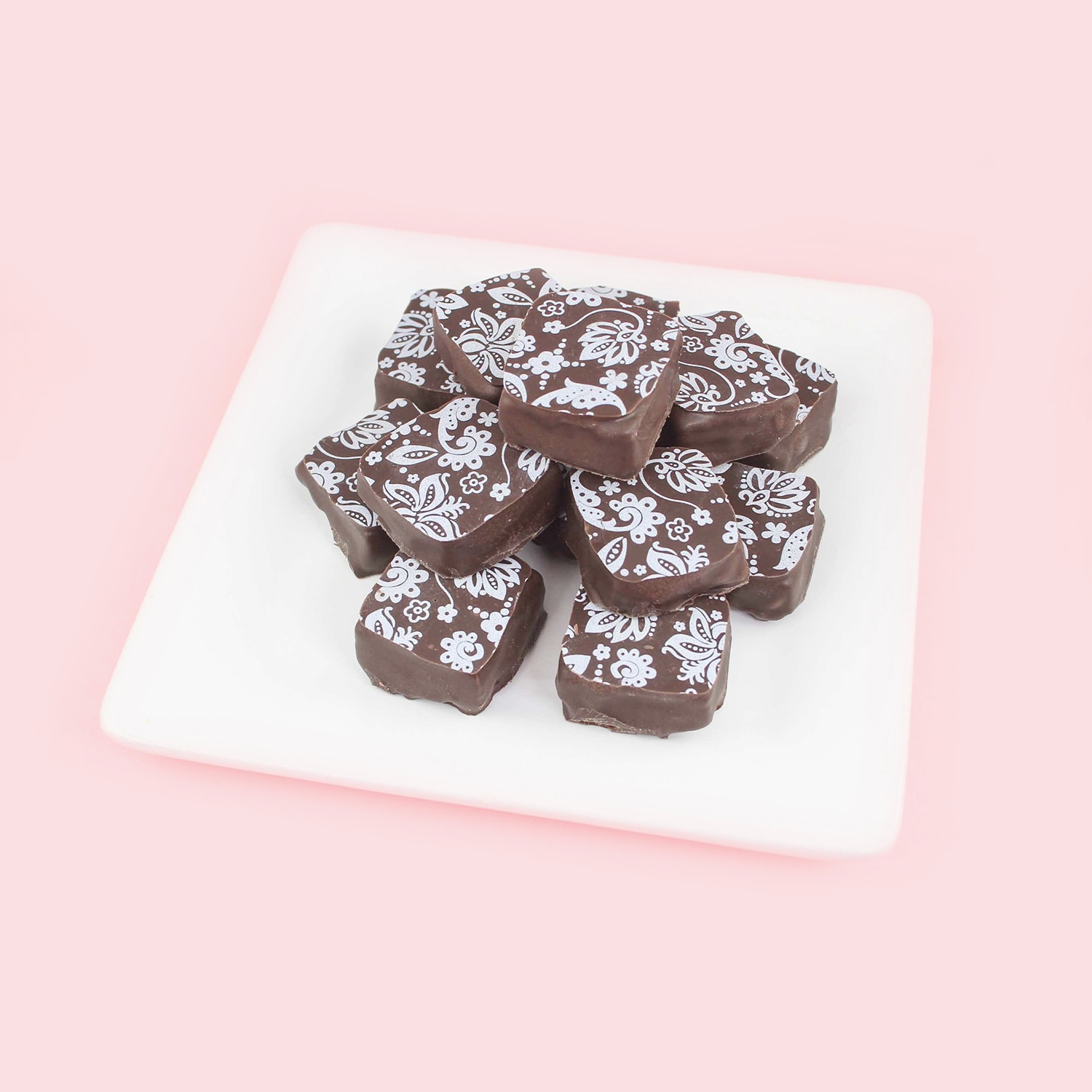 Dipped raspberry ganache squares set up as a pyramid on a white plate.