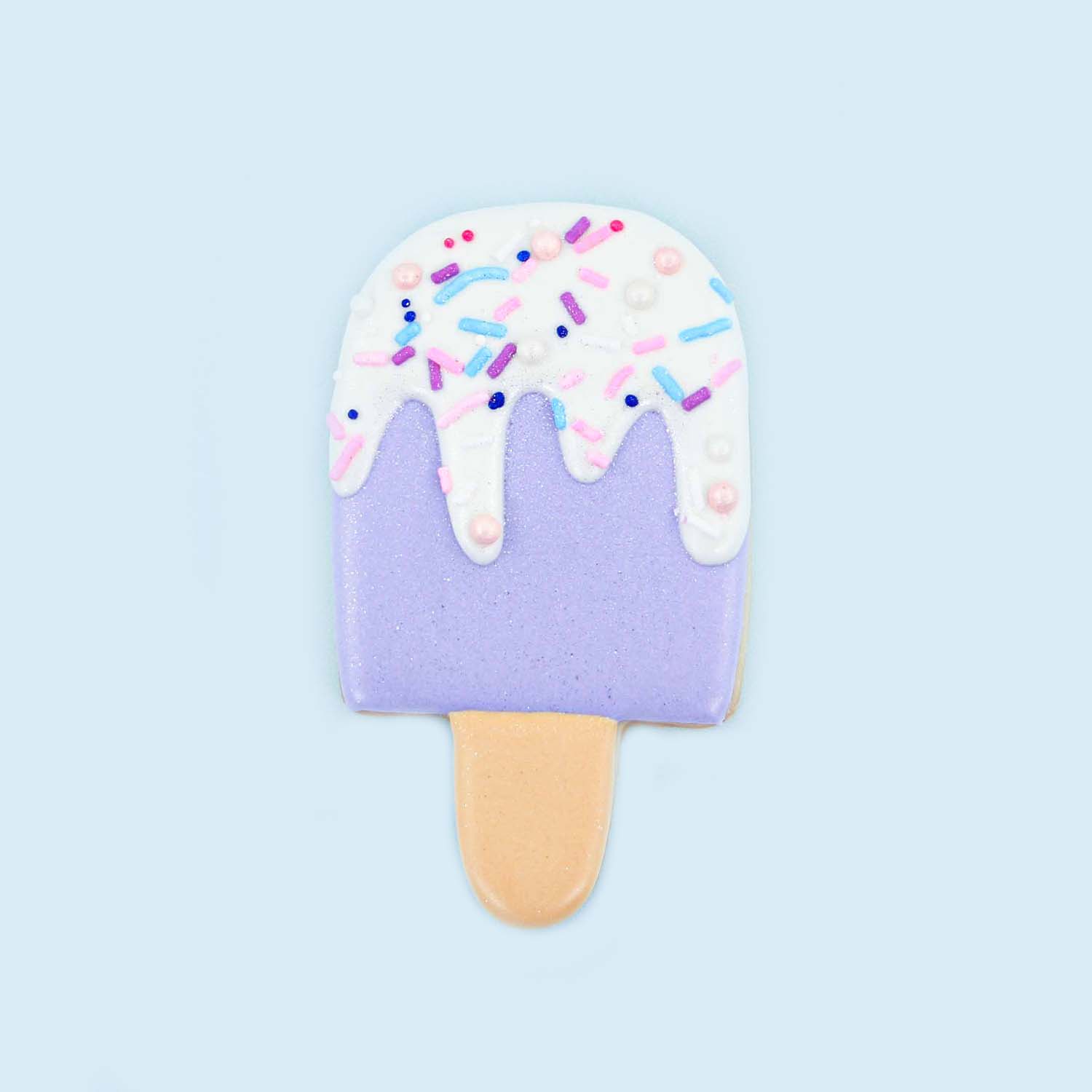 Purple ice cream bar with a white drip and sprinkles cookie decorated with royal icing.