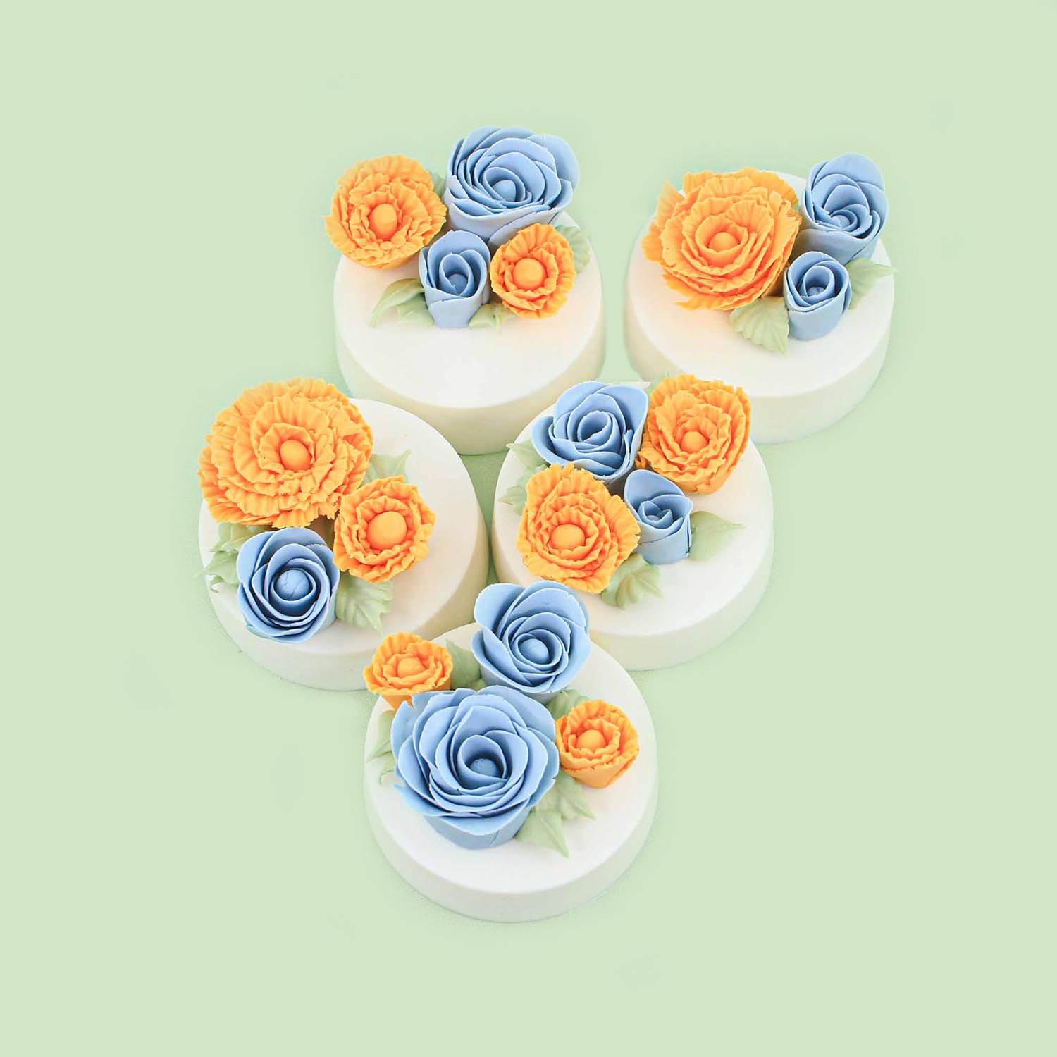 Fondant shaped roses in yellow and blue adorn the top of chocolate covered molded sandwich cookies