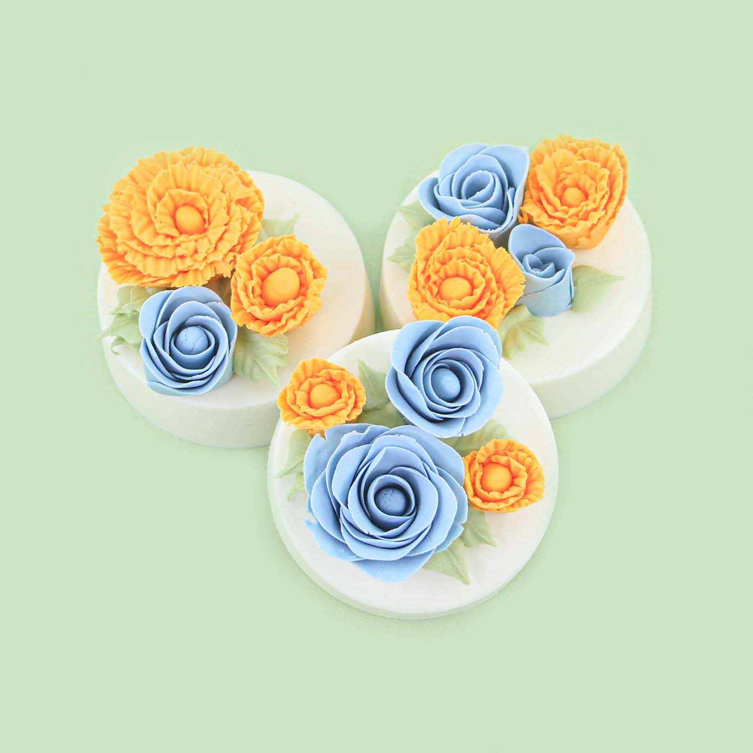 Handmade fondant roses in yellow and blue adorn the tops of chocolate covered molded sandwich cookies.