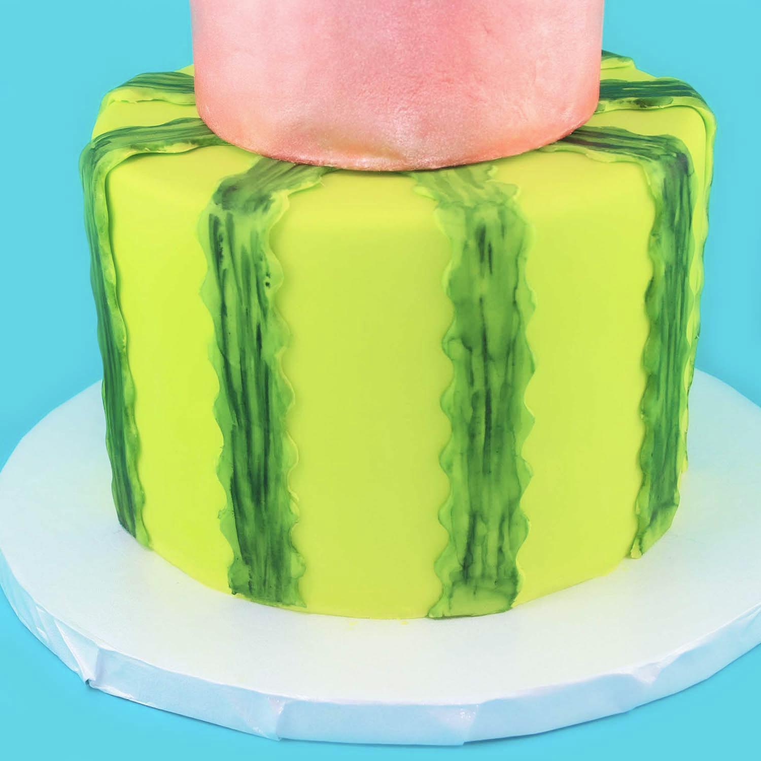 the bottom tier of the watermelon cake covered in bright green fondant and dressed with bright green fondant ribbons hand painted with cypress green food color to represent the variagaged rind of the watermelon.