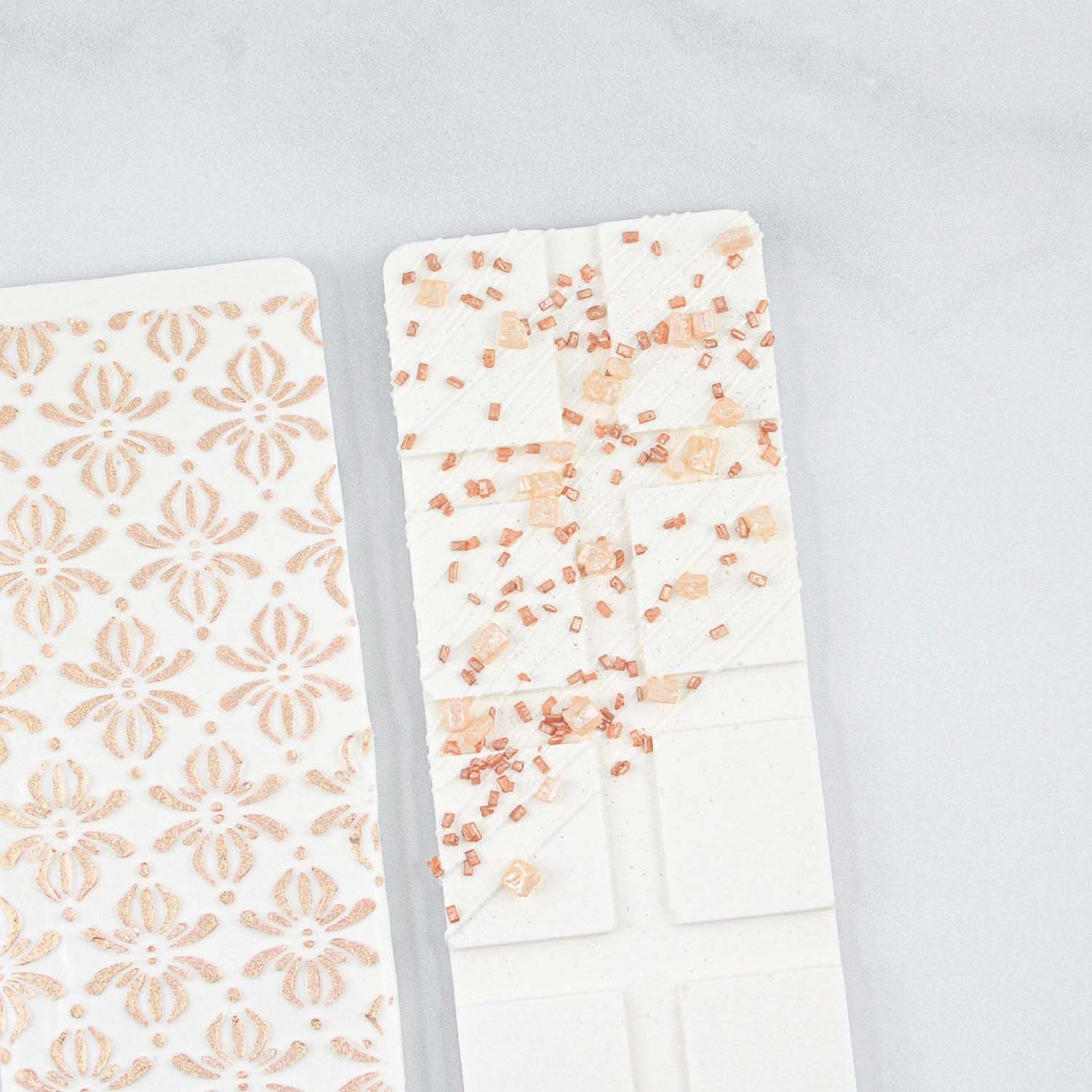 White molded candy bar. Back side is stenciled in rose gold and the front is drizzled with rose gold sprinkles.