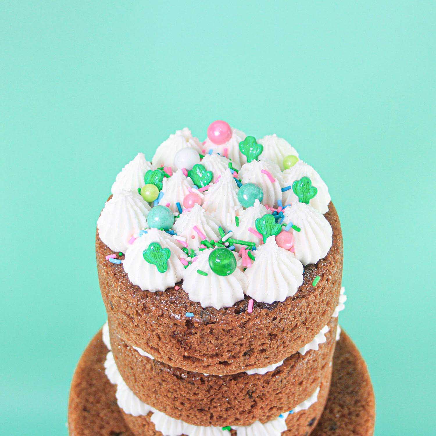 Top of the tiered Cookie Cake with dollops of buttercream, pink and green sprinkls, sugar pearls and candy cactus sparkling with edible glitter.