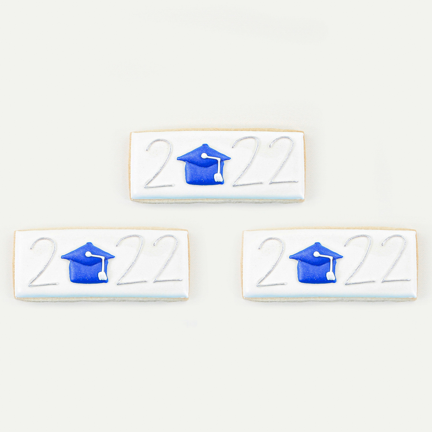 Skinny rectangular cookie decorated in white royal icing with 2022. Blue royal icing graduation cap in place of the 0 in 2022.