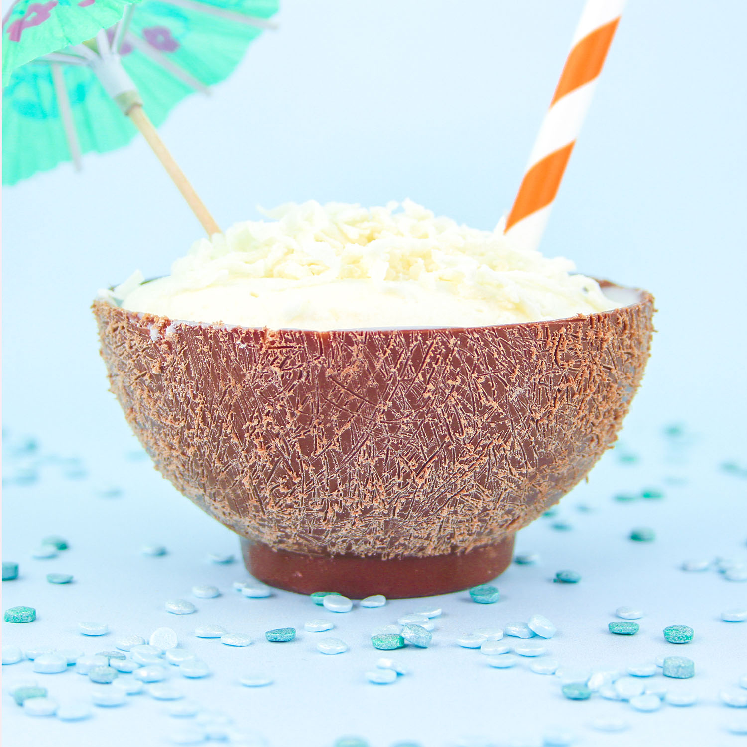 Chocolate Made Dessert cups look like a coconut and filled with a combination of whipped cream and rum flavoring, coconut pastry filling flavored with pineapple and sprinkled with coconut, a straw and cocktail umbrella.