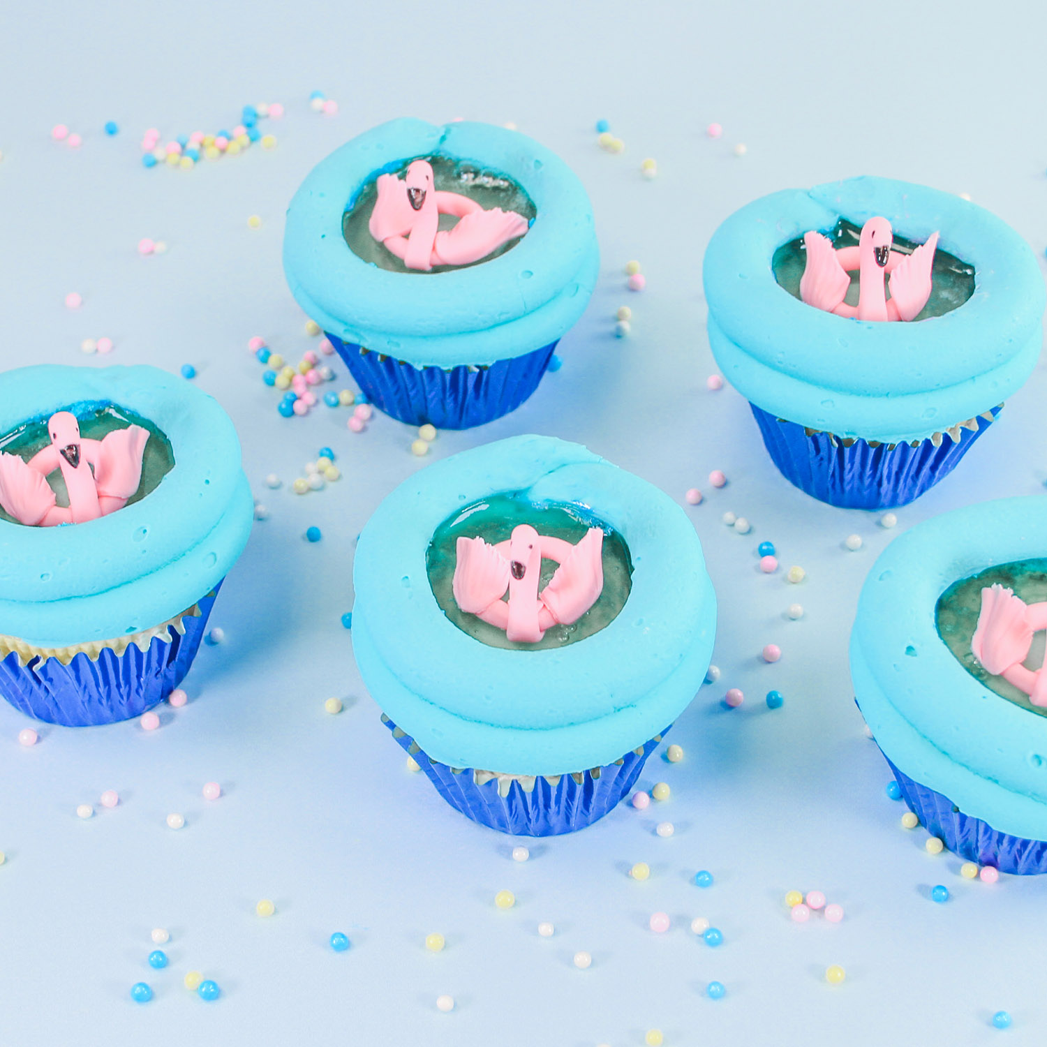 Blue buttercream piped on a cupcake to resemble a round pool. Filled with blue gelatin for water and topped with a fondant made pink flamingo floaty