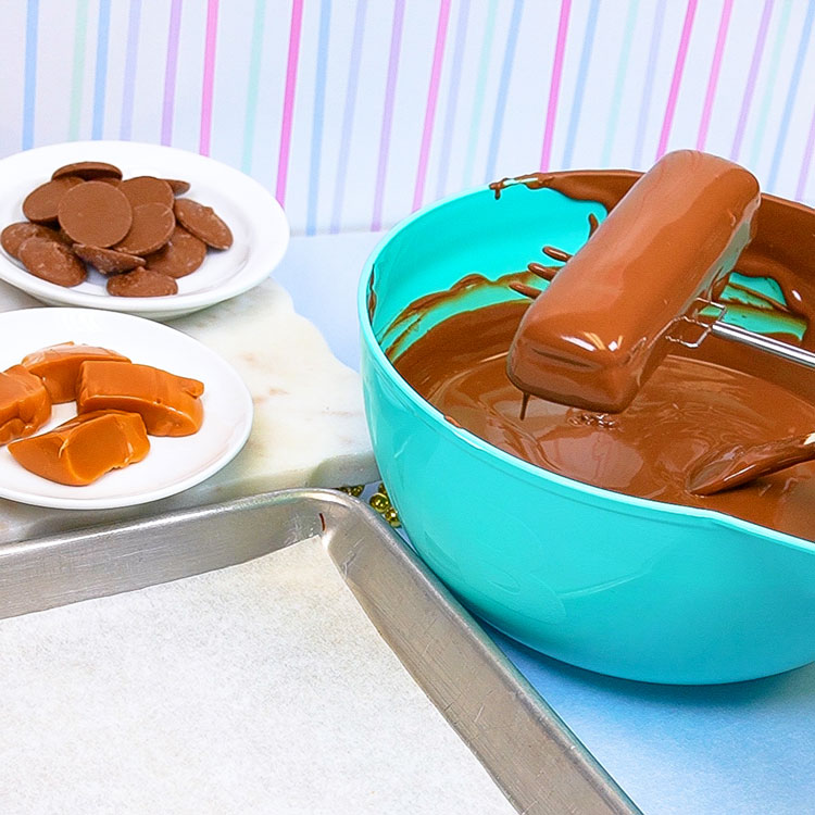 dipping caramel shortbread cookie into melted milk chocolate