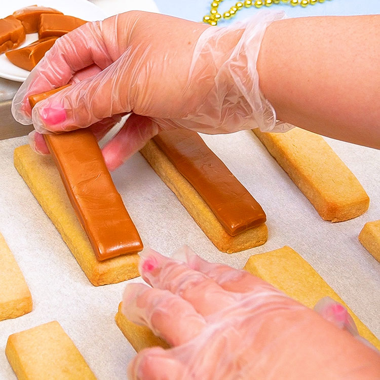 putting peters caramel onto baked shortbread cookies