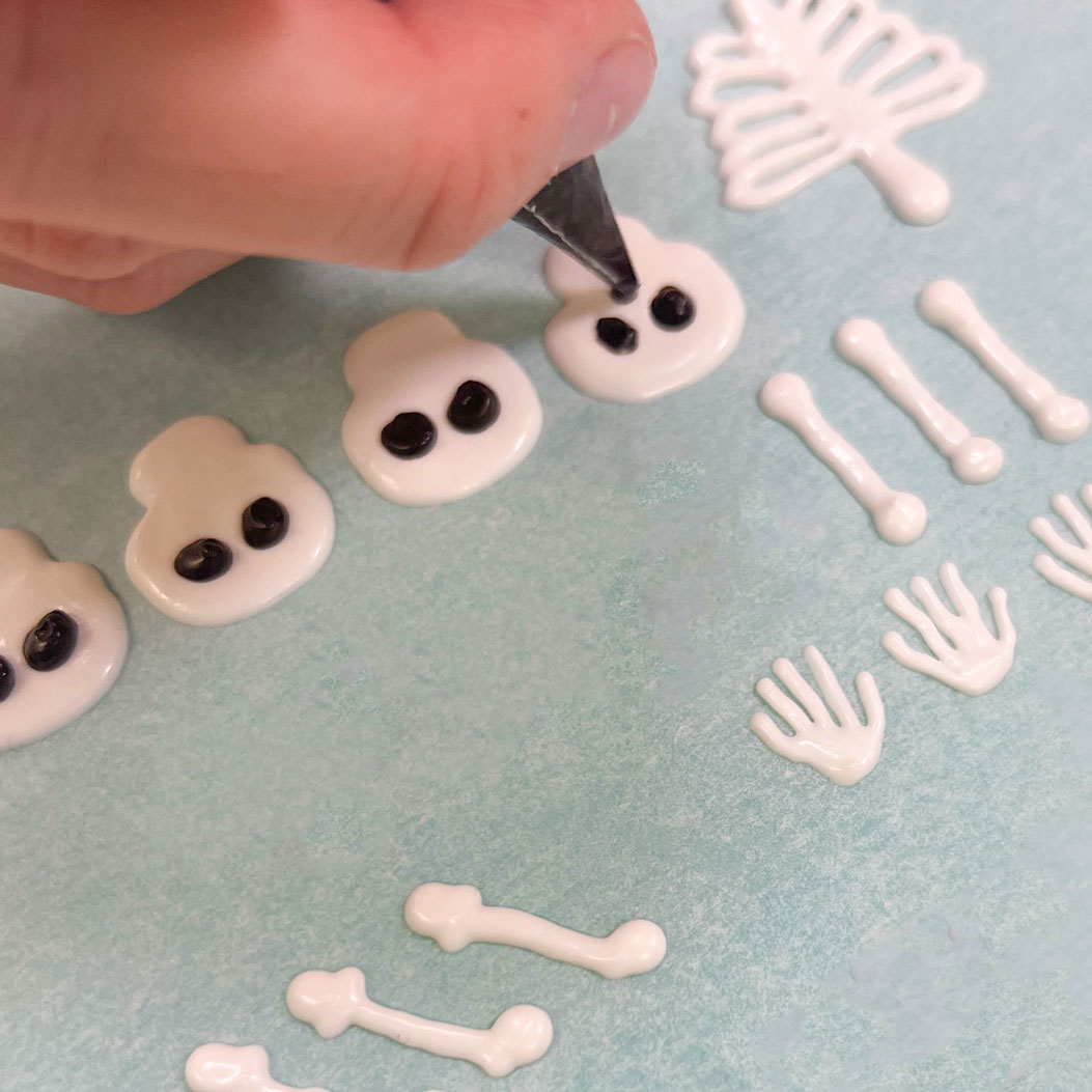 piping black chocolate onto white chocolate skeletons