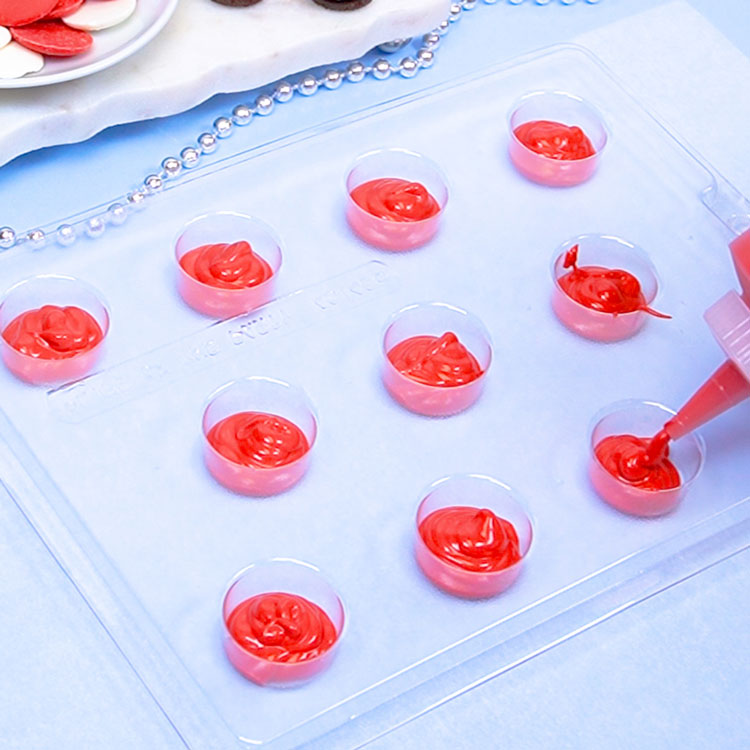 filling mini oreo chocolate mold with melted red chocolate