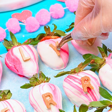 adding chocolate letter to strawberry using tweezers