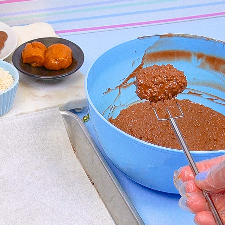 dipping caramel into tiny crisp rice and chocolate mixture