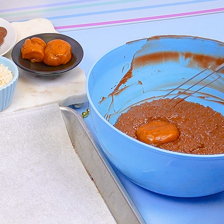 dipping caramel into tiny crisp rice and chocolate mixture