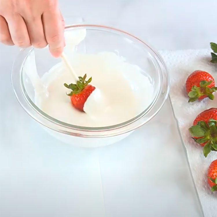 dipping a strawberry into melted white chocolate