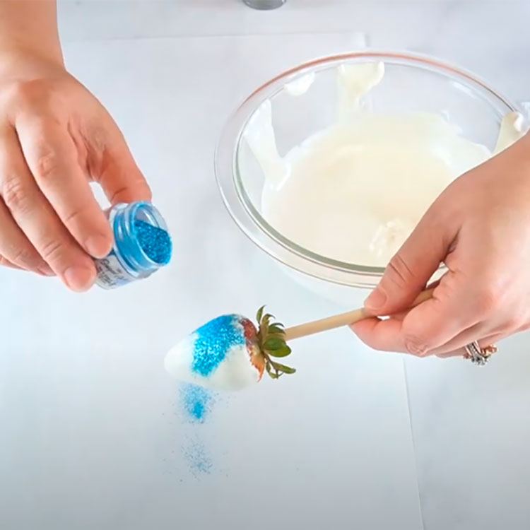sprinkling edible blue glitter onto a chocolate coated strawberry