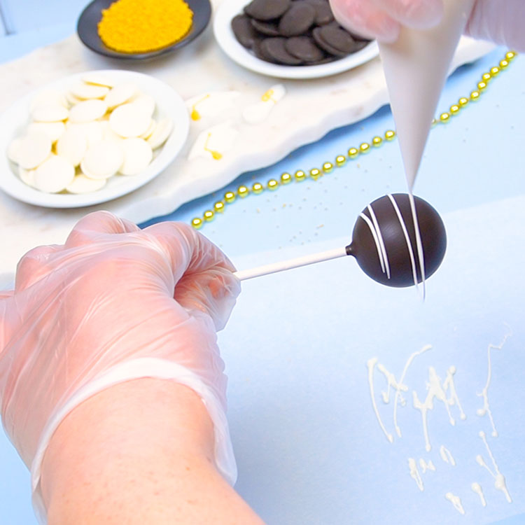 adding white chocolate drizzle to a cake pop