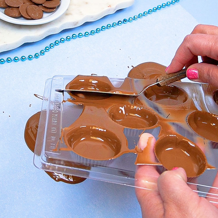 scraping top of mold to remove excess chocolate using an angled spatula