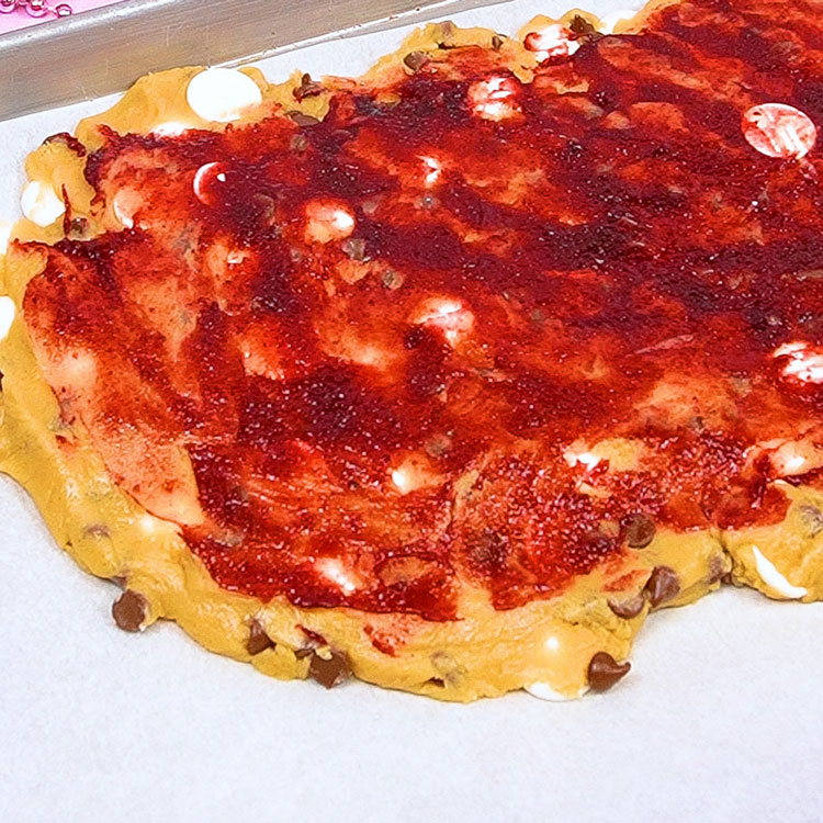 spreading raspberry icing fruit on top of cookie dough