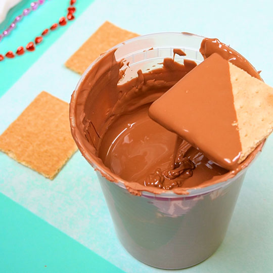 dipping graham cracker into melted milk chocolate