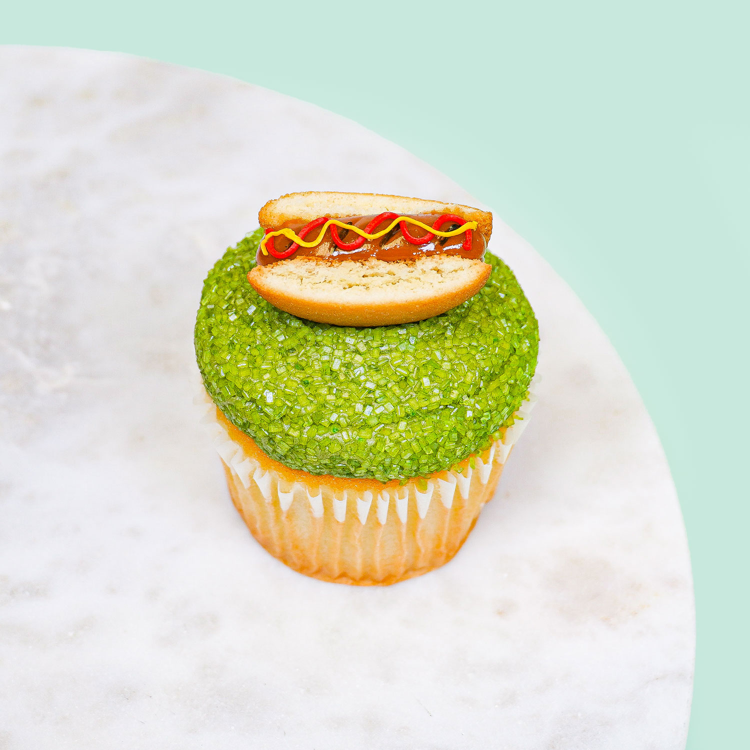 cupcake decorated to look like a hot dog sitting on grass