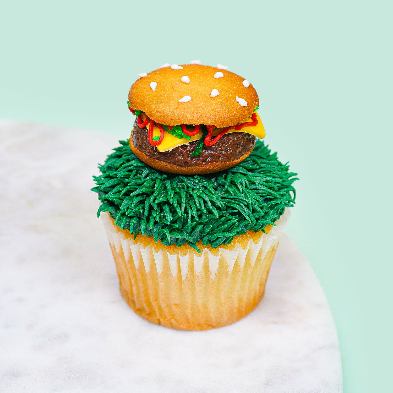 cupcake decorated to look like a burger sitting on grass